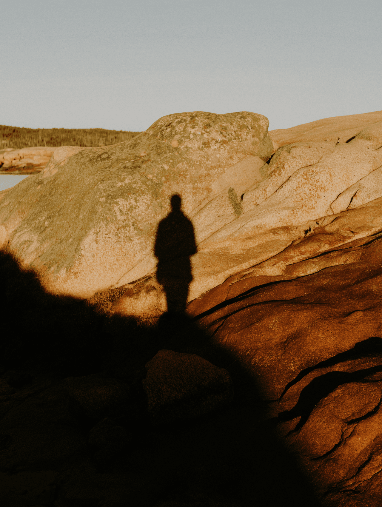 Long shadow of a standing person cast across sunlit rocky terrain at golden hour.
