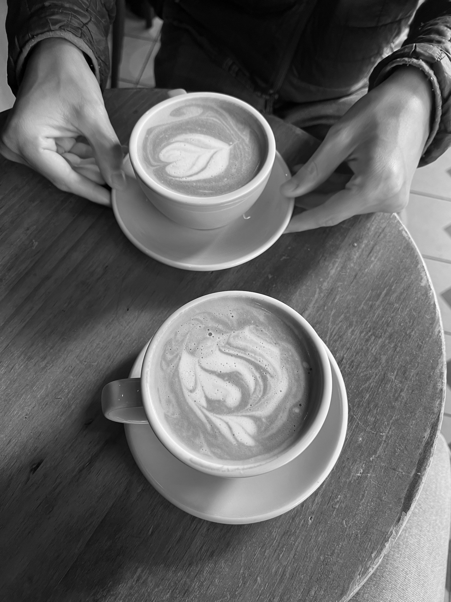 Two latte coffees on a table with two hands holding one of the coffees