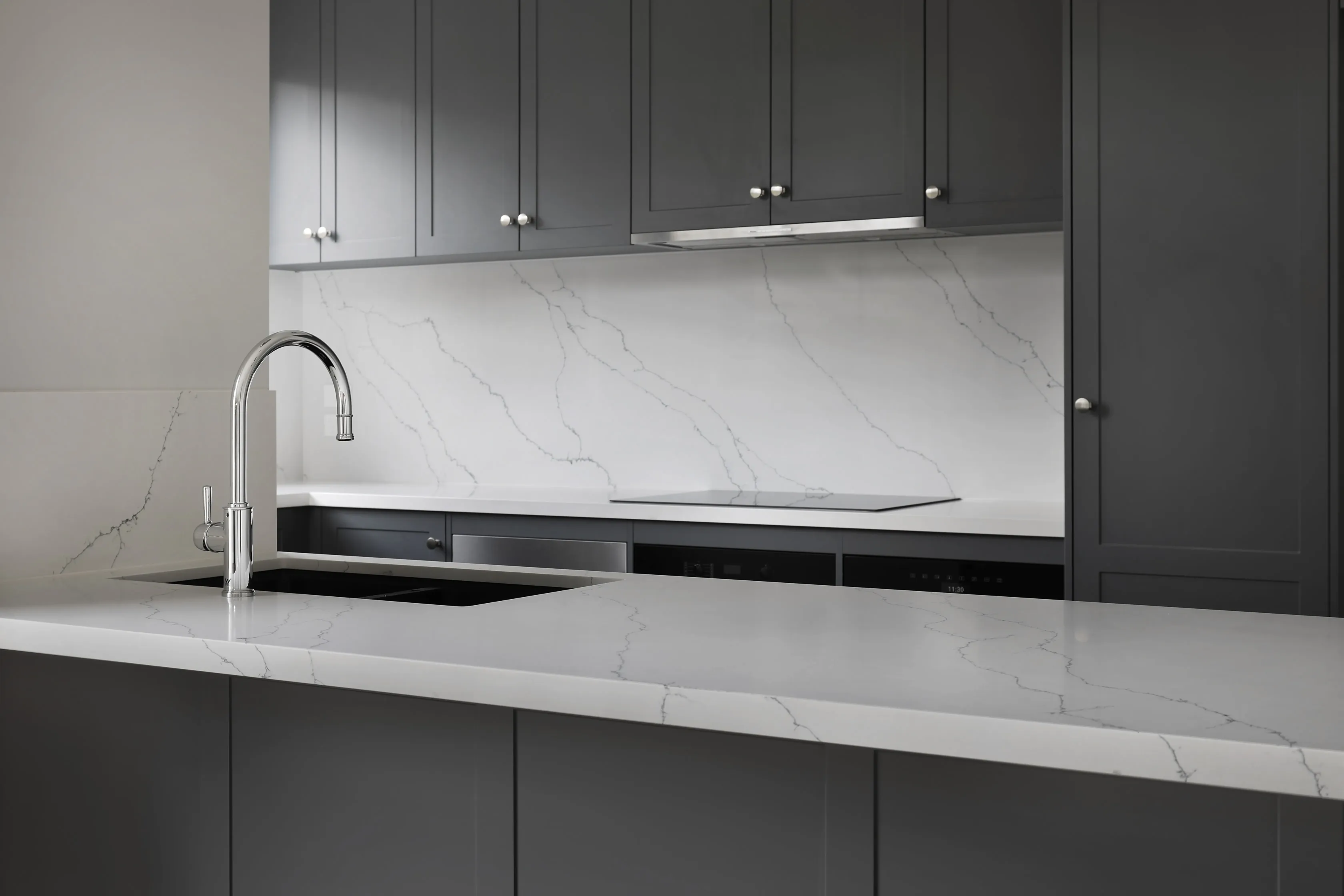 Charcoal kitchen detail with a book-matched Calacatta marble splashback and waterfall benchtop, chrome gooseneck tap, integrated cooktop and dark shaker cabinetry