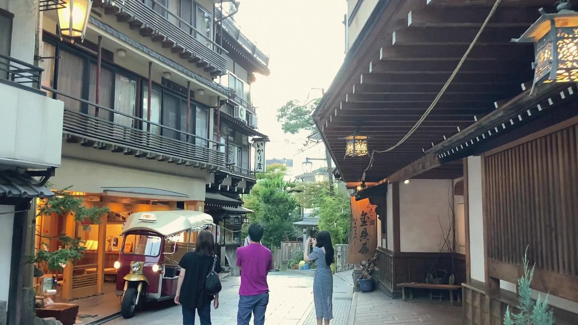 Visitors stroll a lantern-lit stone lane in Shibu Onsen at dusk, past wooden ryokan and a vintage cart.