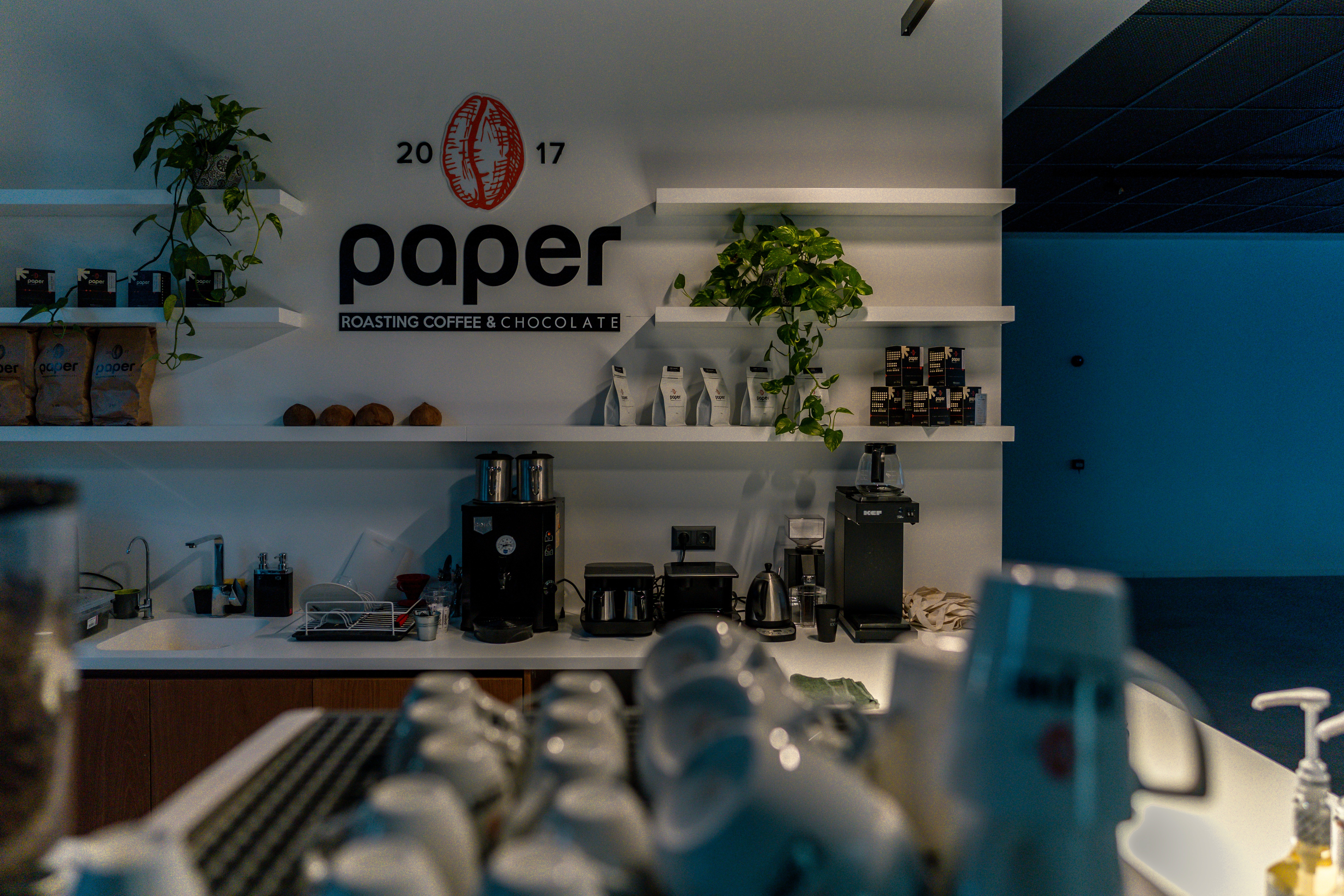 Cozy coffee corner inside Ikas Office featuring Paper Coffee Roasters branding, minimalist white shelves, and espresso equipment setup.