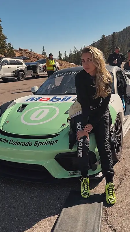 Emelia Hartford stands next to a bright green Porsche sports car with a Mobil 1 decal across the hood on a sunny day.