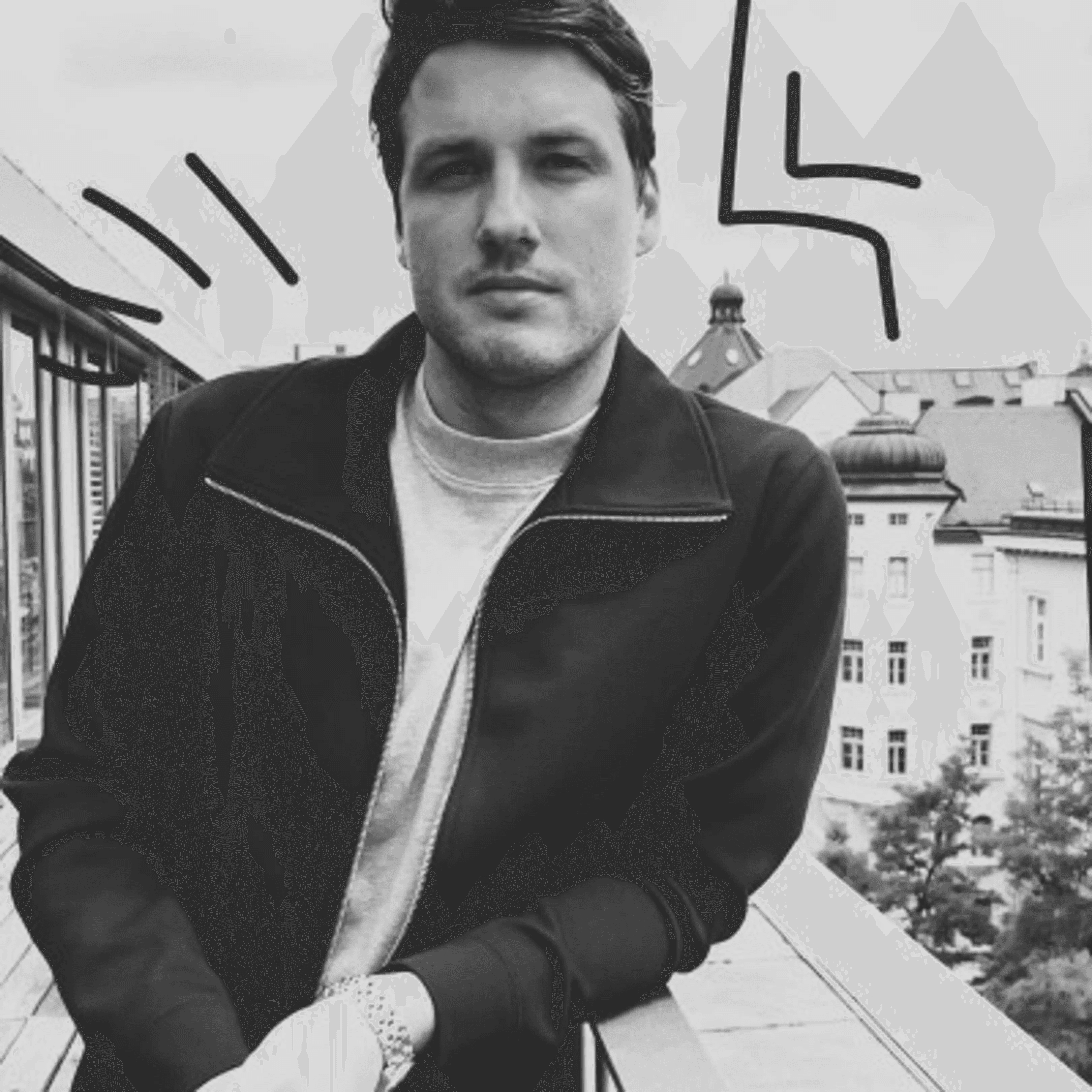 A smiling person with curly hair sits at a desk with computers in a stylish, well-lit office setting.
