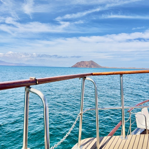 Boat deck with railing overlooking calm blue sea and distant island under a partly cloudy sky.