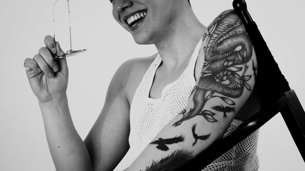 Black-and-white close-up of the tattooed upper arm of a young man laughing