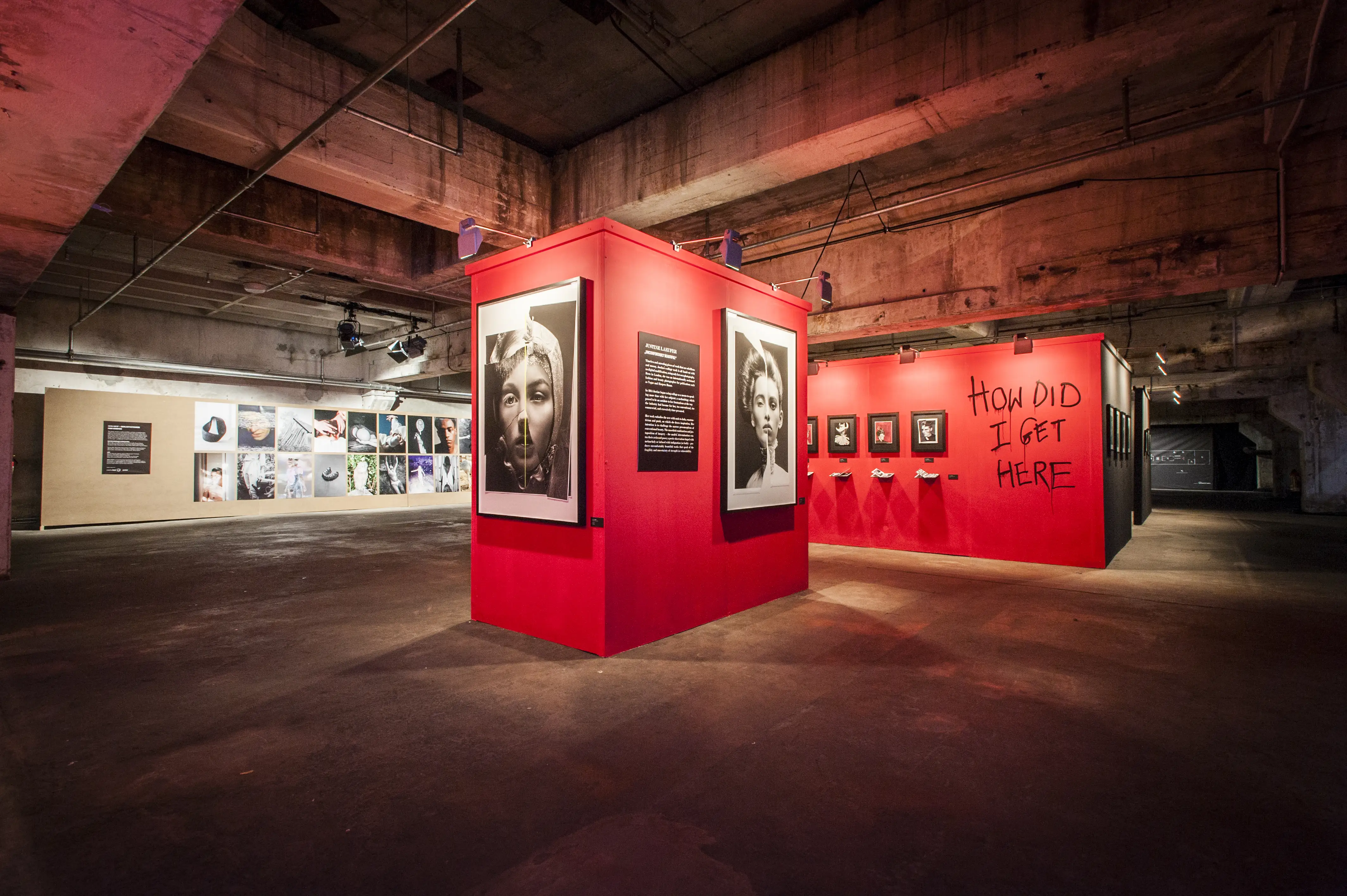 Red exhibition cube with large black-and-white portraits and a wall scrawled with How Did I Get Here at BERLIN PHOTOWEEK in the raw Kraftwerk hall.