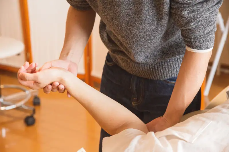 Chiropractor performing a manual wrist and forearm assessment on a patient during a muscle reactivation evaluation