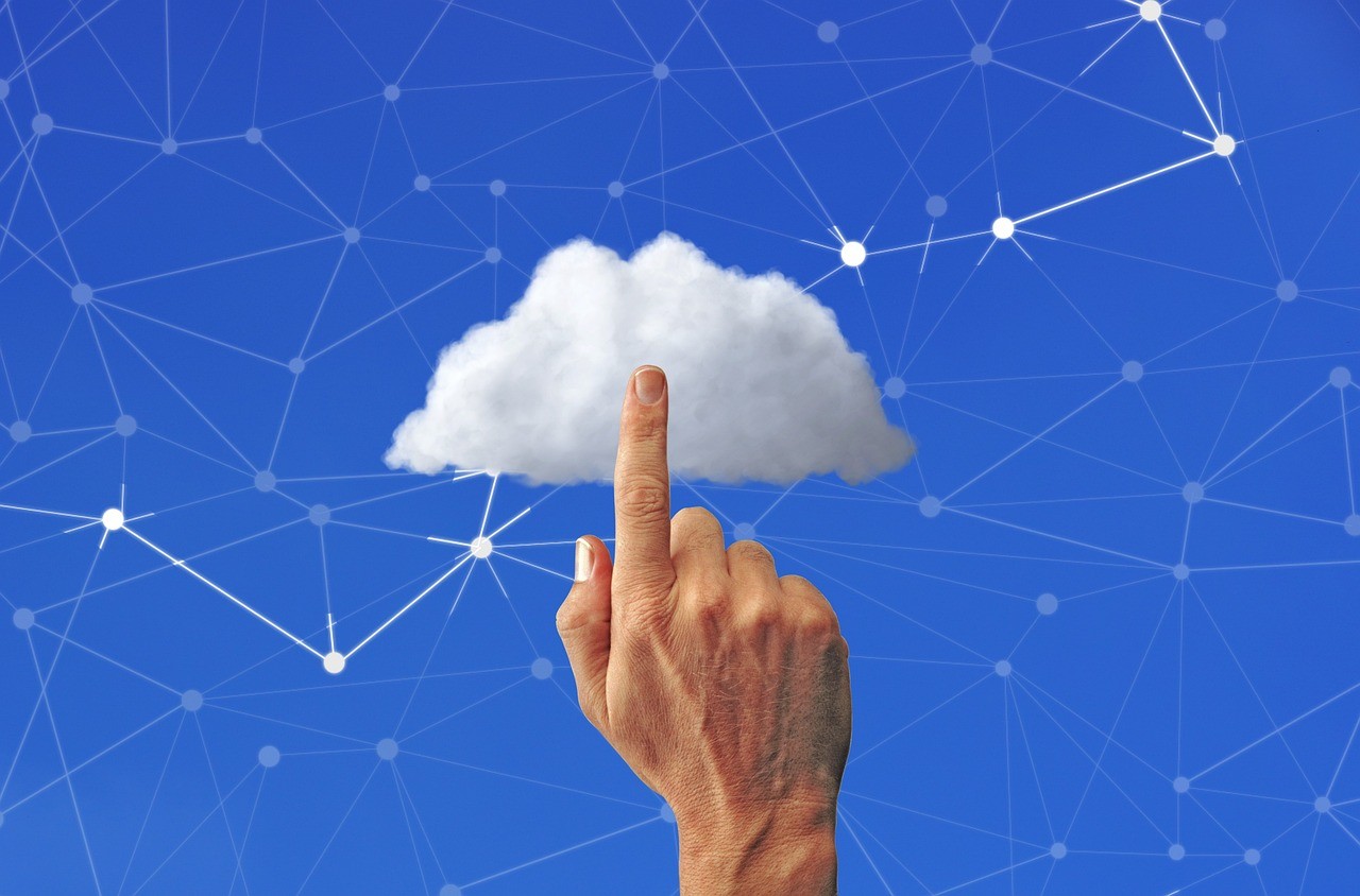 Hand pointing to cloud icon on blue digital network background representing cloud computing and online data storage