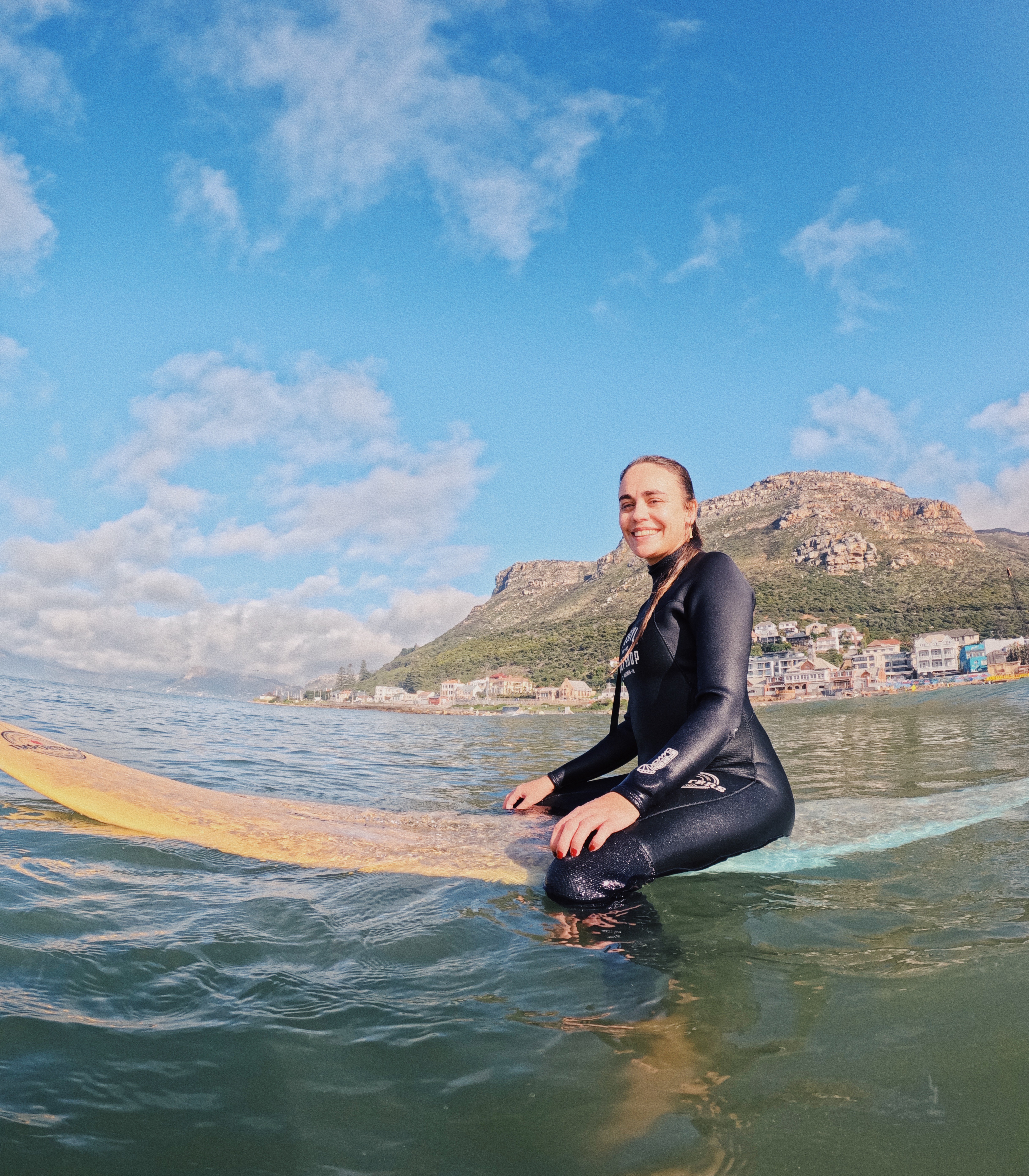 A female beginner surfer sitting on her surfboard smiling during her beginner surf lesson in Muizenberg, Cape Town