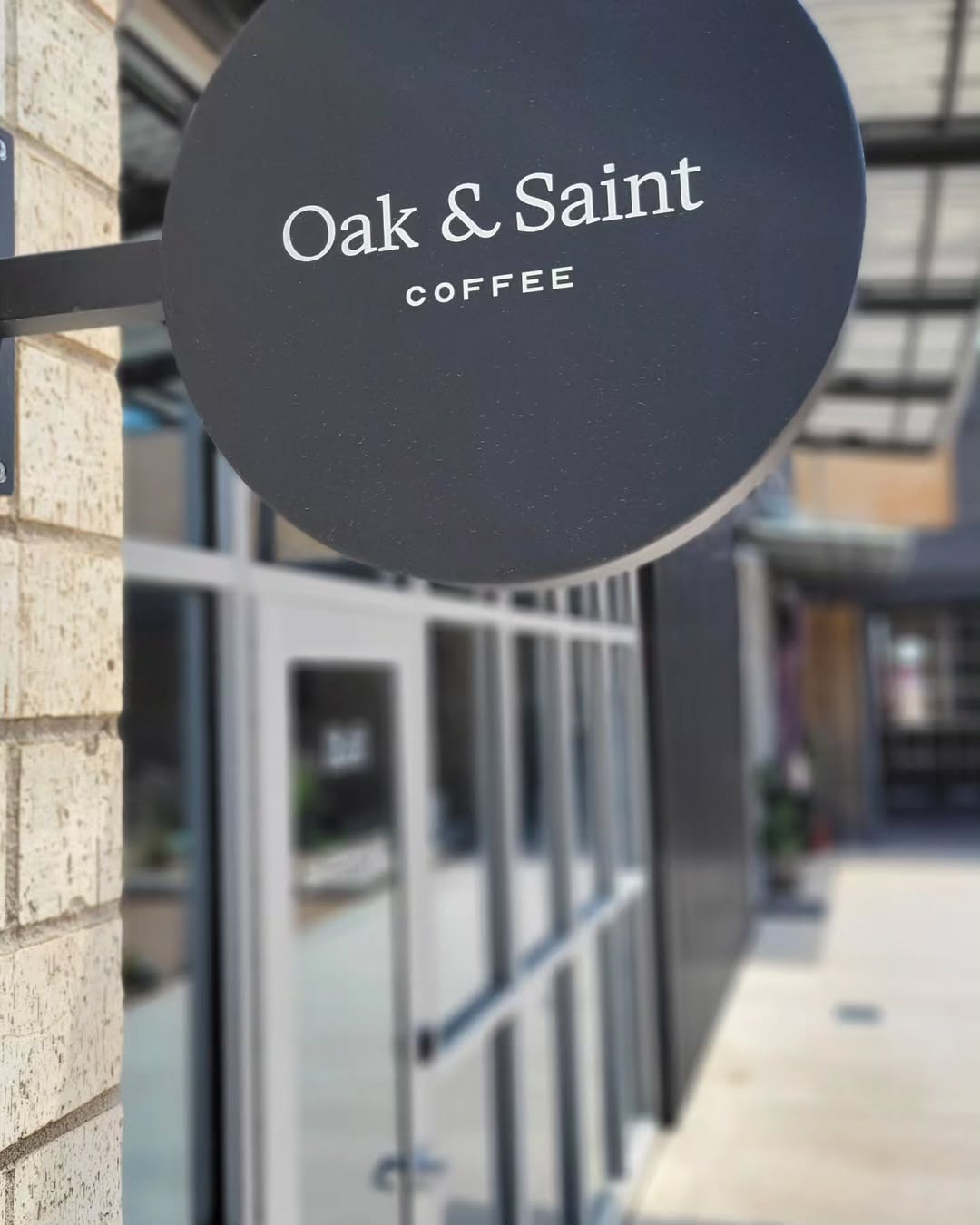 Round exterior blade sign for Oak & Saint Coffee mounted on brick storefront.