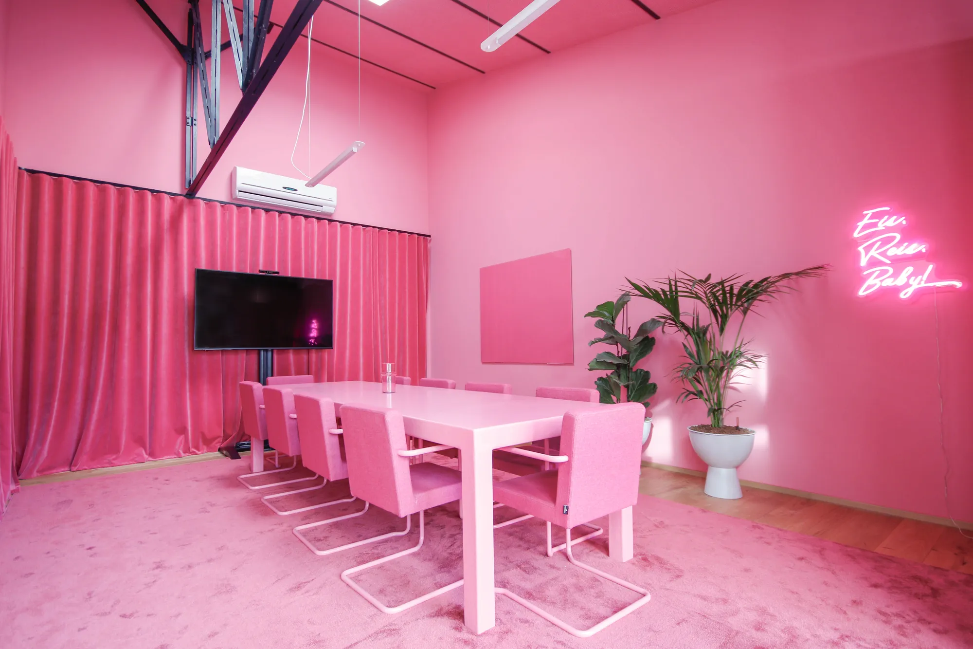 All-pink meeting room with velvet curtains, table, chairs and a neon Eis Reis Baby sign.