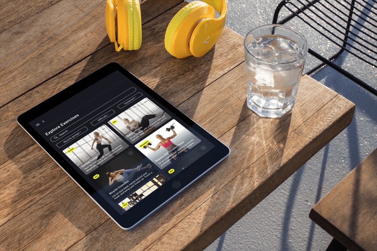 Mockup image of tablet sitting on wooden table next to cup of water and yellow headphones