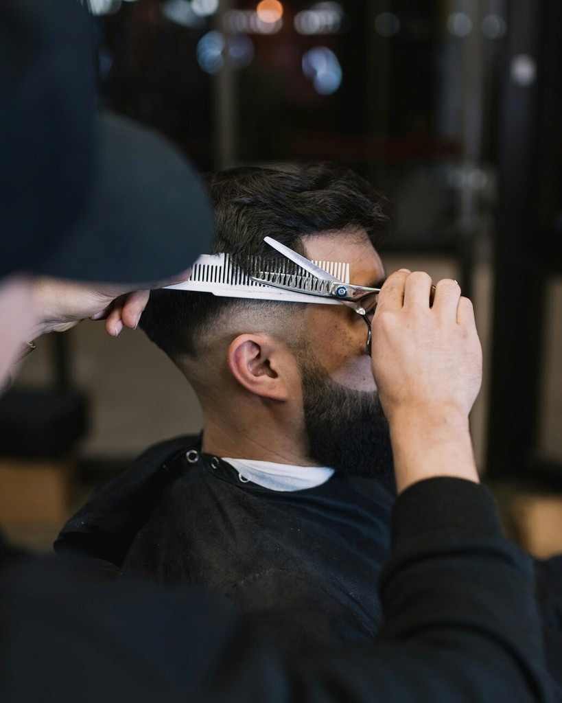 Classic Pompadour Haircut in a Barbershop: A barber in a classic white shirt and black apron giving a stylish pompadour haircut to a male client in a traditional barbershop setting.