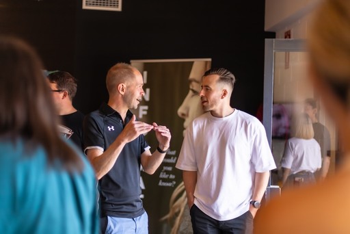 A group of four people standing outside a building, engaging in conversation, with cars parked nearby.