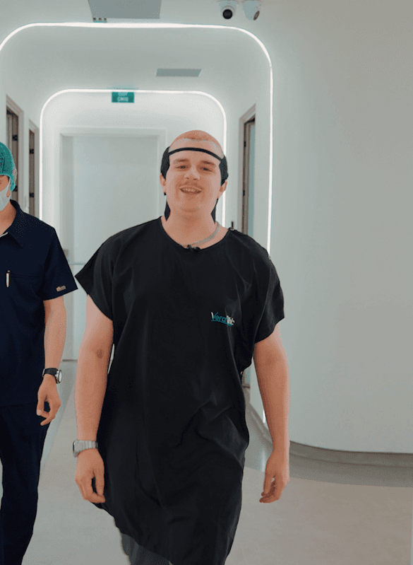 A young man smiling confidently in a clinic hallway, wearing a post-op headband after a hair transplant procedure at Vera Clinic. Marks the turning point in the narrative, showcasing the accessibility and positive experience of the treatment process.