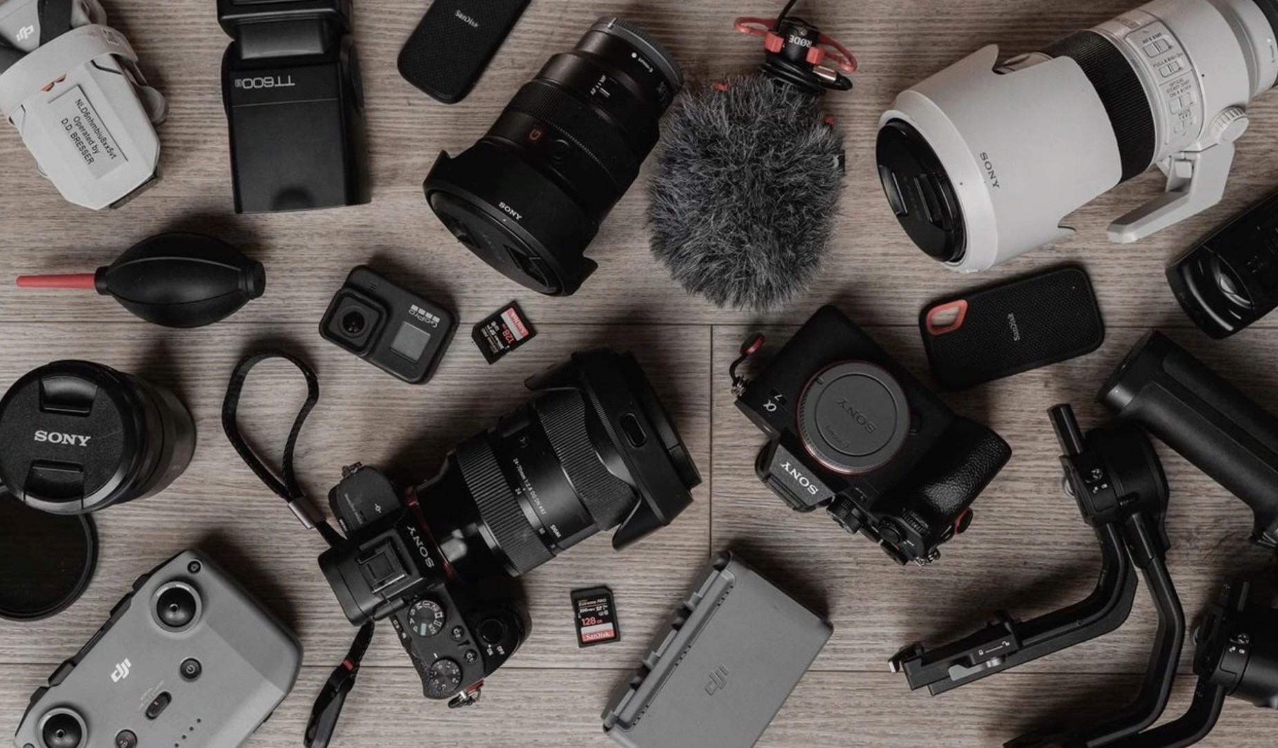A black Leica camera with a textured body is dramatically lit in red, reflecting on a glossy surface. The red background adds a bold, intense mood.