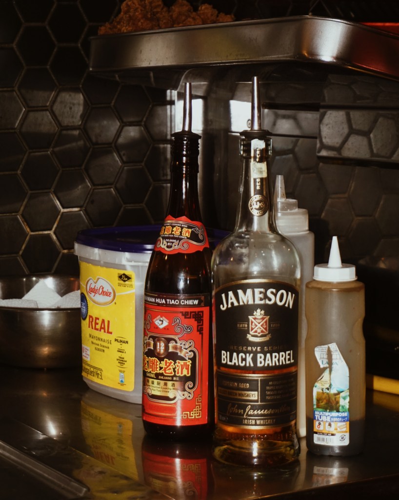A selection of sauces and condiments on a kitchen counter, featuring a bottle of Jameson Black Barrel whiskey, a traditional Chinese sauce, mayonnaise, and a multipurpose condiment bottle.