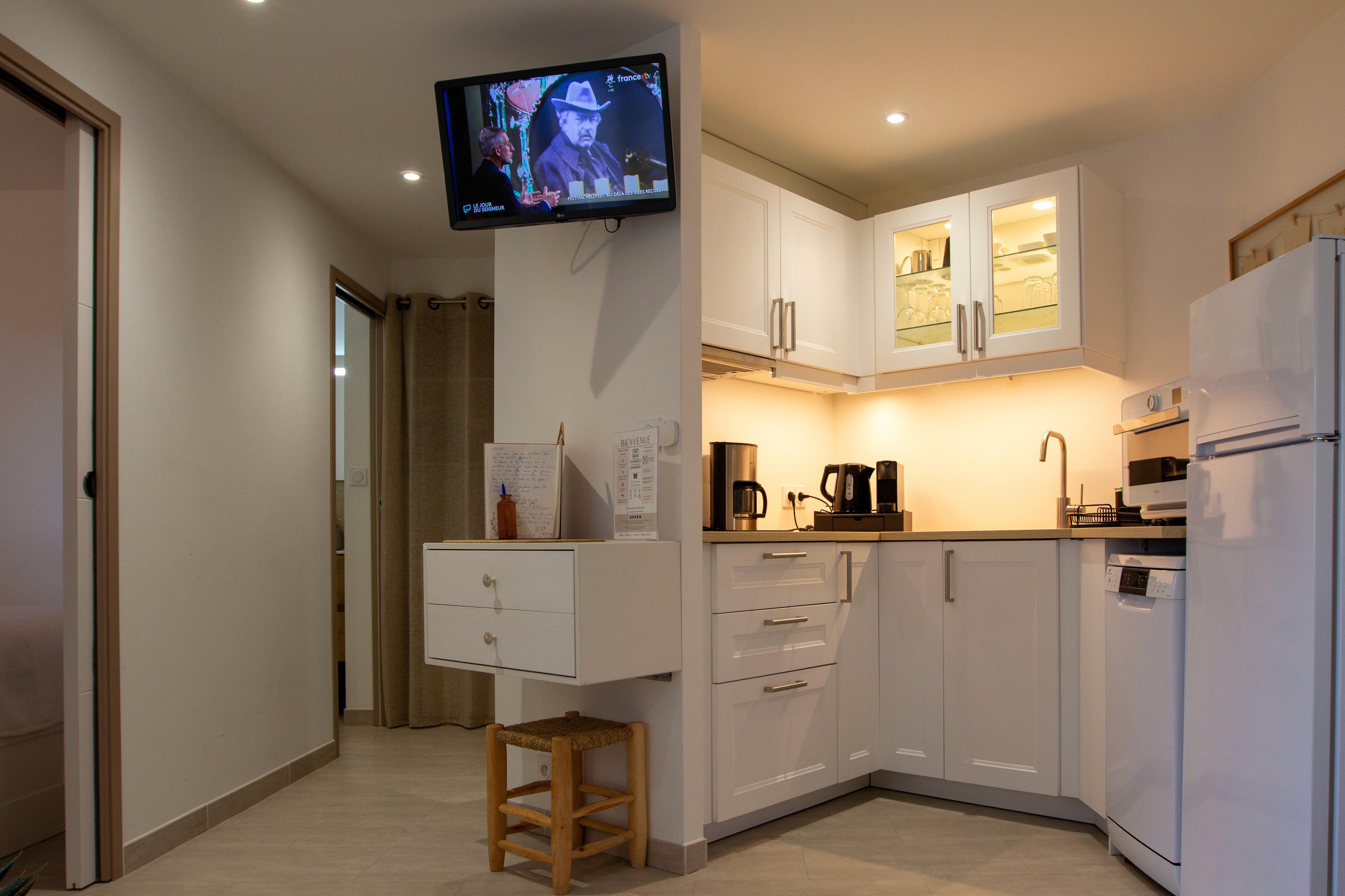 Petite cuisine équipée blanche et bois moderne avec électroménager complet et éclairage sous meuble.