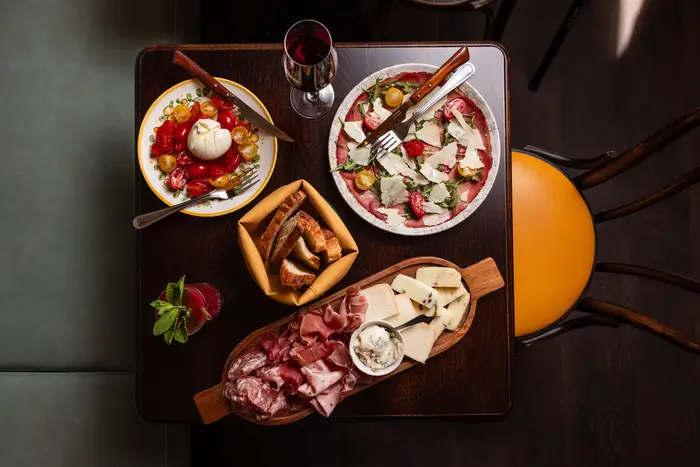 Assiette d’antipasti italiens avec charcuterie, produits frais tomates cerises & burrata, grand carpaccio de boeuf, accompagné d'un vin italien de choix ainsi que d'un cocktail fruité.