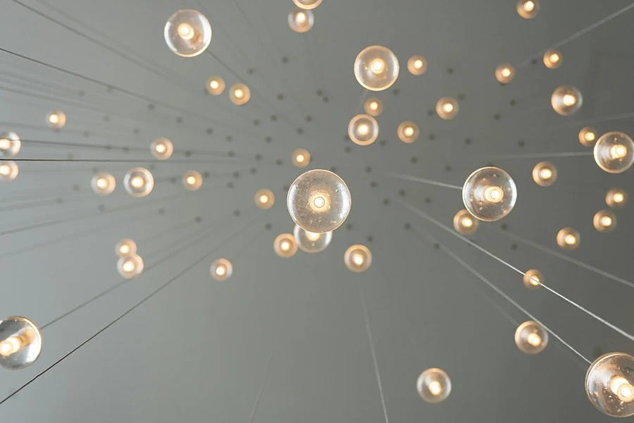 A ceiling view of multiple hanging round light bulbs glowing warmly, suspended by thin wires at varying lengths, symbolizing creativity, bright ideas, and innovation.