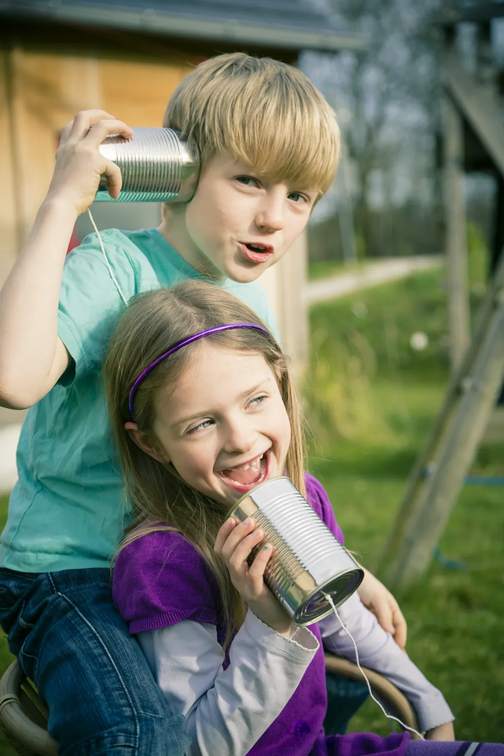 two children speaking to each other using tin cans and string
