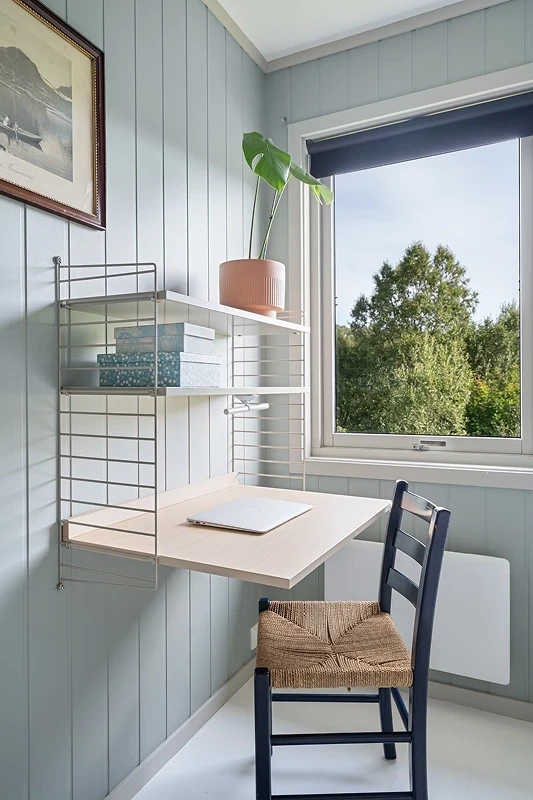 A space-saving home office nook with a wall-mounted desk and shelving system on a light blue shiplap wall.