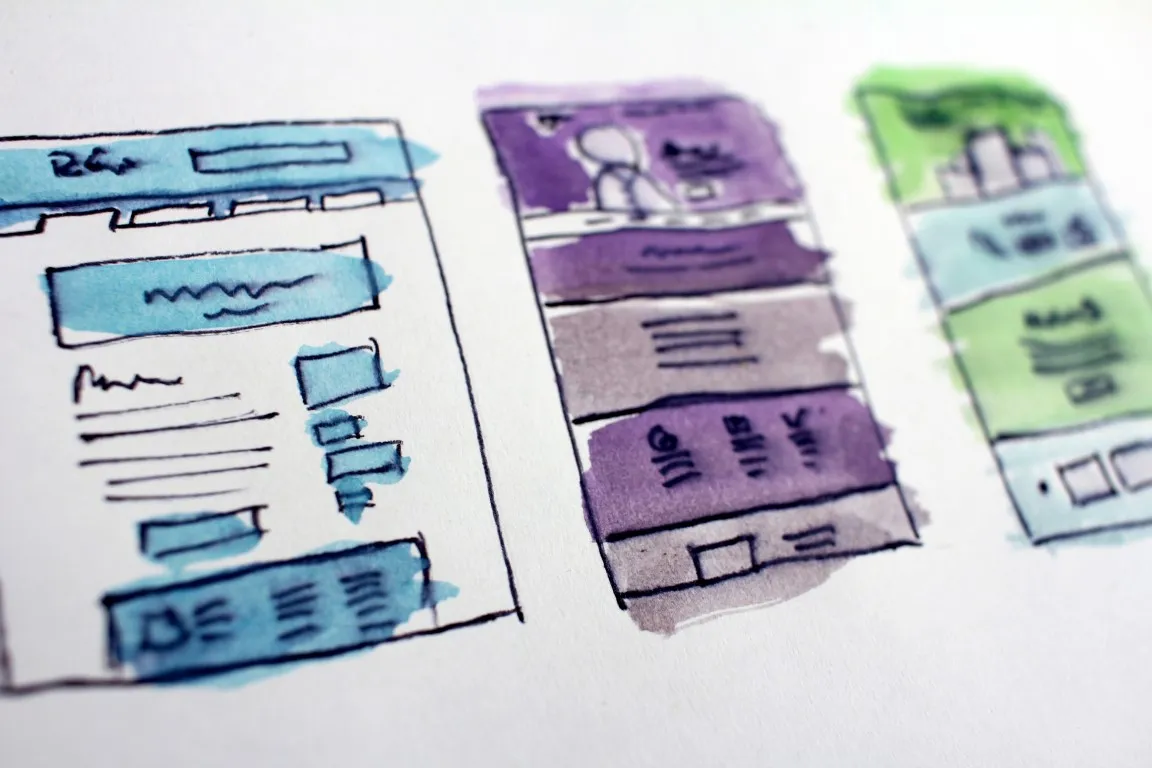 Three hand-drawn user interface (UI) wireframes or website mockups on paper, sketched with blue, purple, and green watercolor washes, illustrating the early stages of web design or UX prototyping.