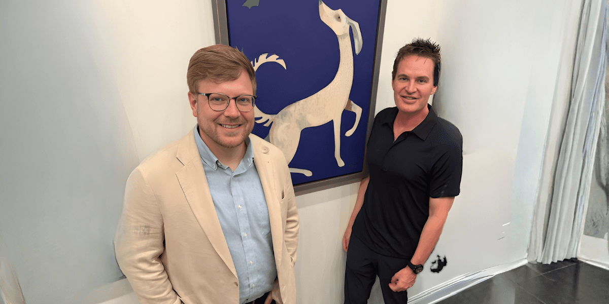 Brett Campbell and another man stand beside artwork of a white dog, representing his role connecting artists and collectors.