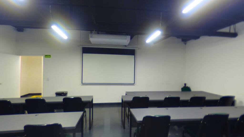 Sala de aula da UNEED com mesas, cadeiras e tela de projeção