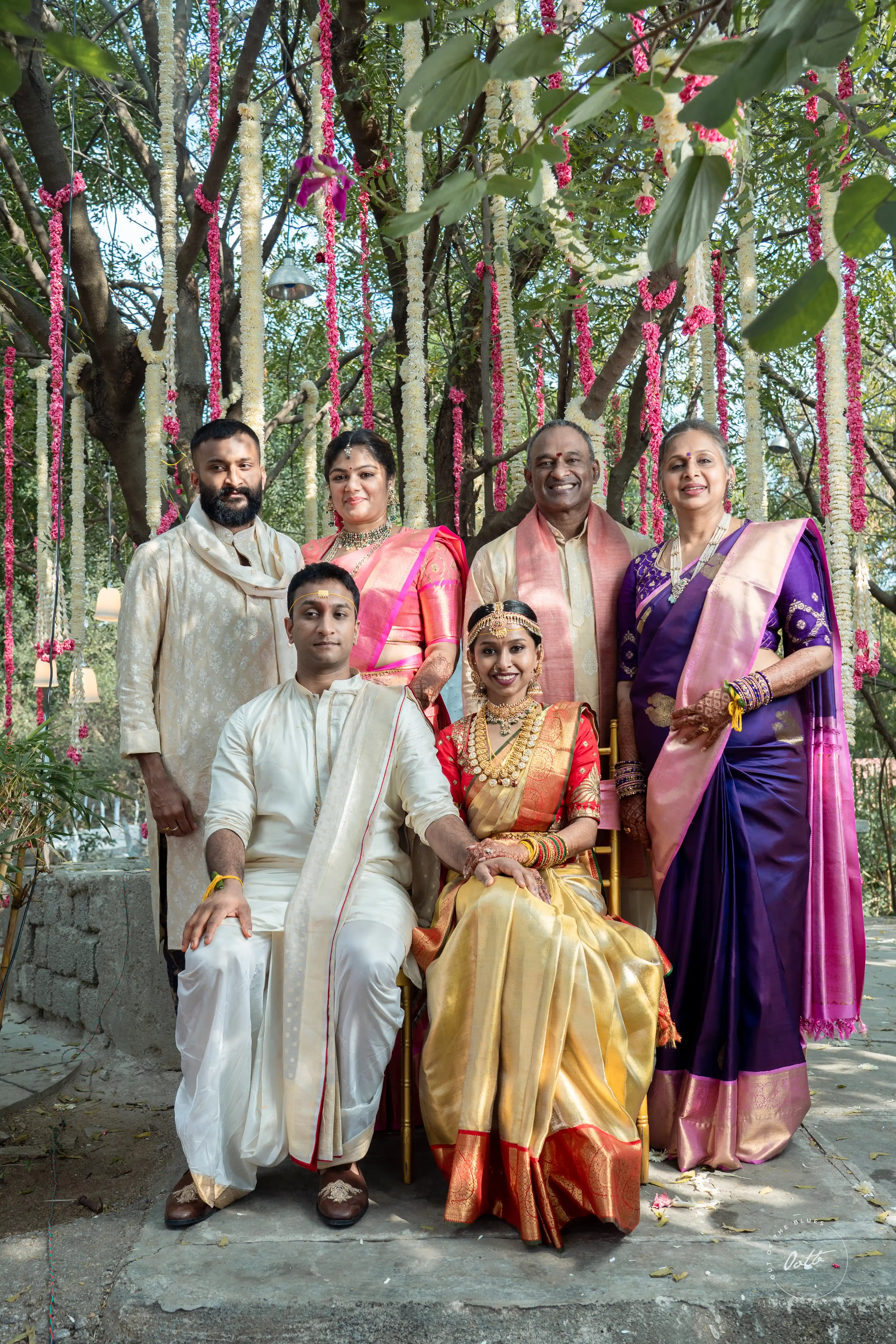 Bride, groom, and family pose together in traditional Indian clothing, surrounded by intricate floral decorations, embodying a classic family shot captured by Out of The Blues Fine Art Wedding Photography in Hyderabad.