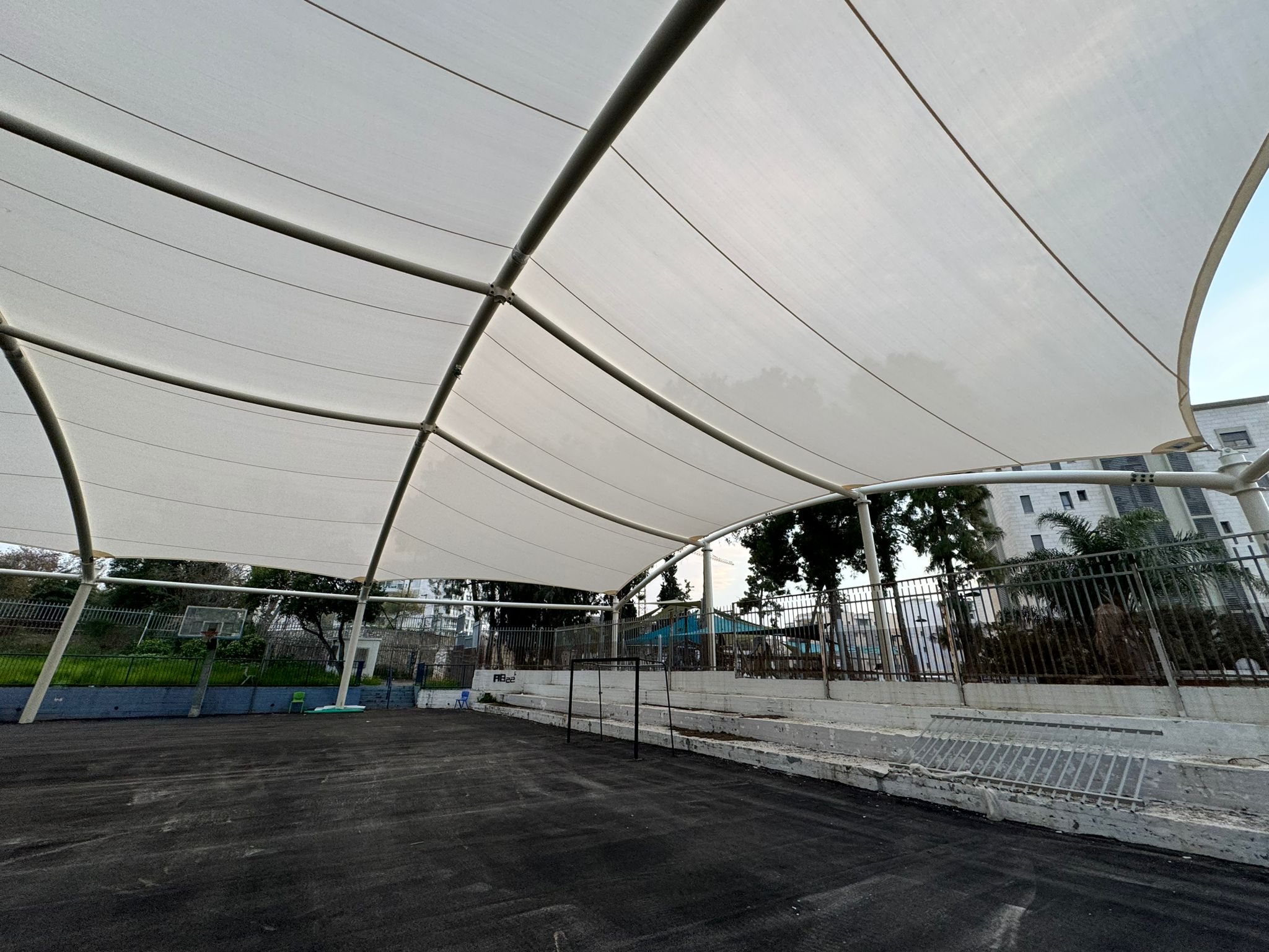 Covered open sports court with surrounding fence under a beige curved membrane structure.