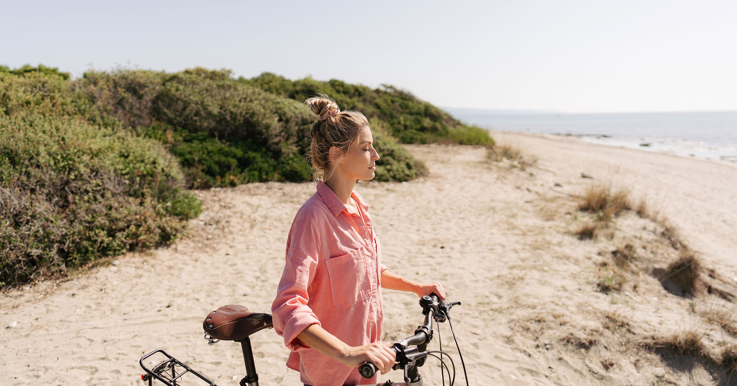En kvinne holder på sykkelen sin på stranden mens hun står med lukkede øyne og nyter stillheten.