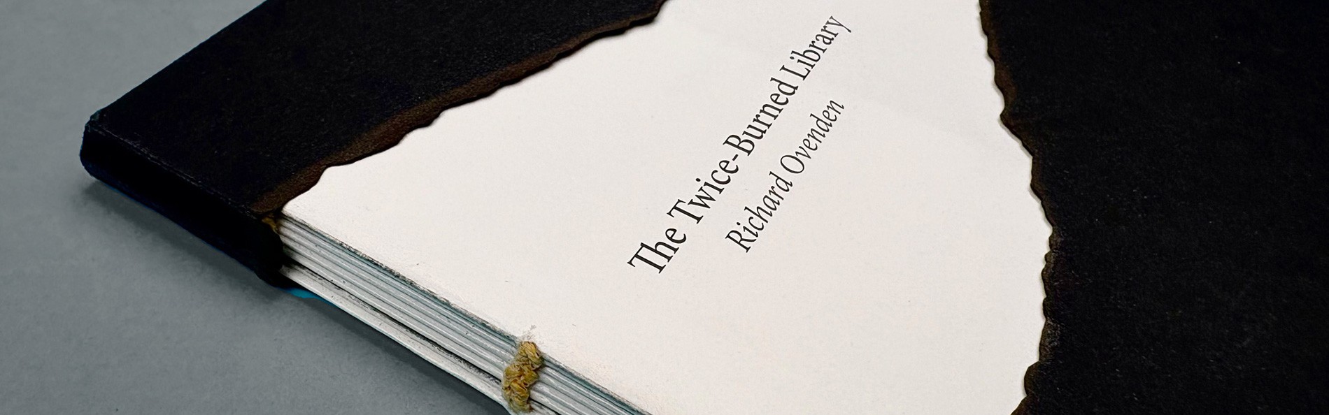 Een schuin bovenaanzicht van het boek. De cover heeft duidelijk afgebrande randen en de fragiele bindingen zijn zichtbaar, wat het kwetsbare karakter van de inhoud weerspiegelt.