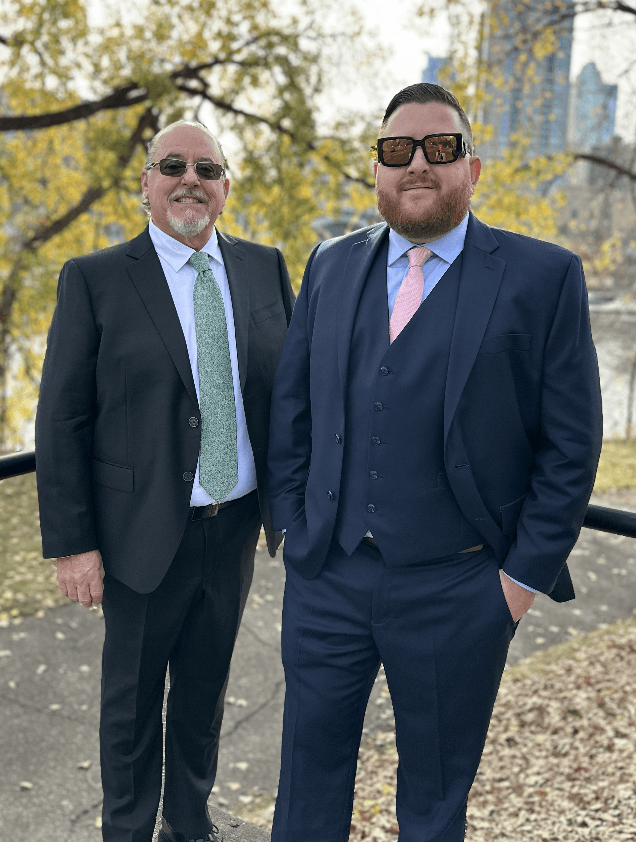Man with short hair and beard wearing a dark blazer and black shirt against a plain background.