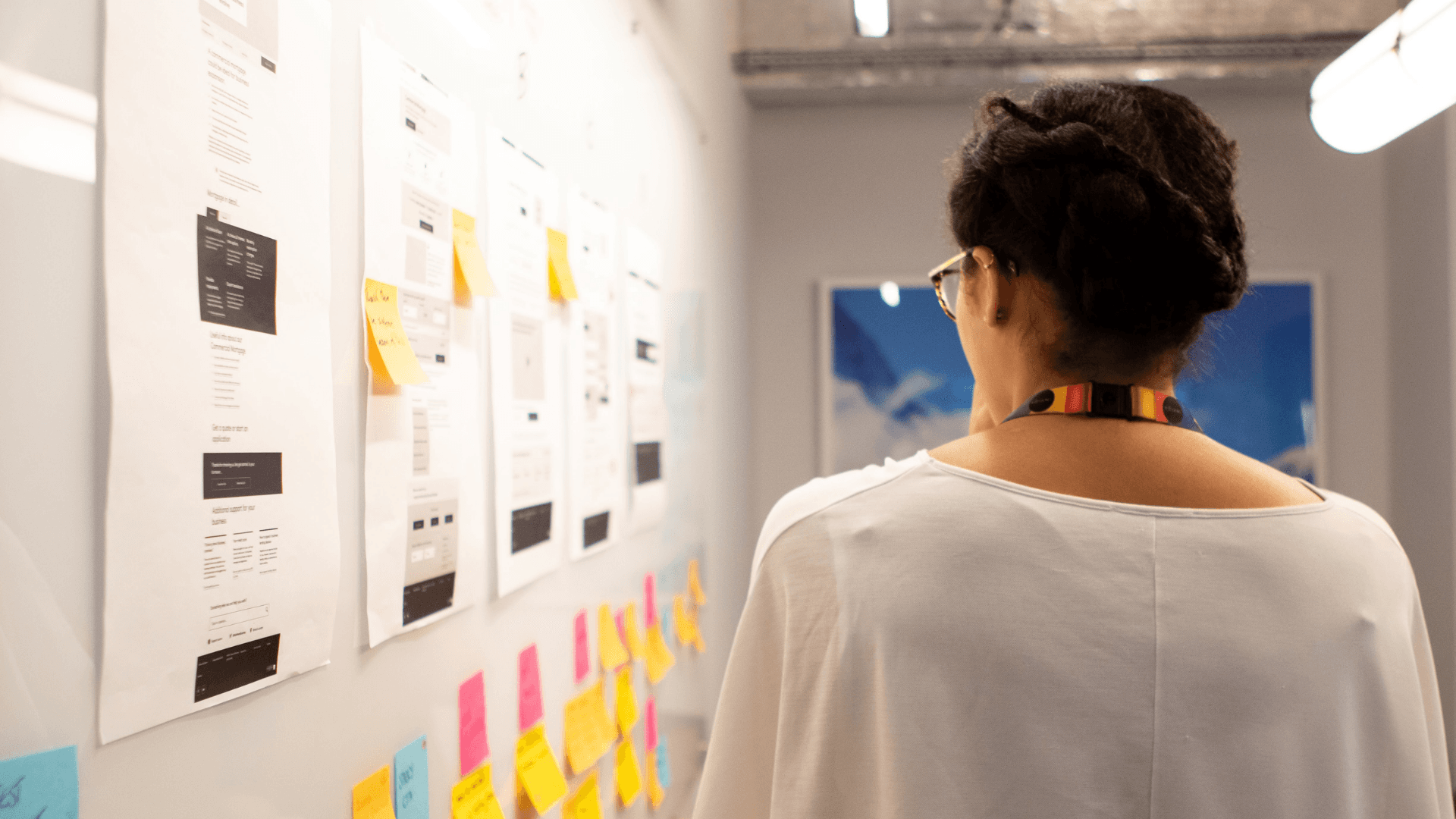 A woman perusing a wall plastered with sticky notes and wireframes
