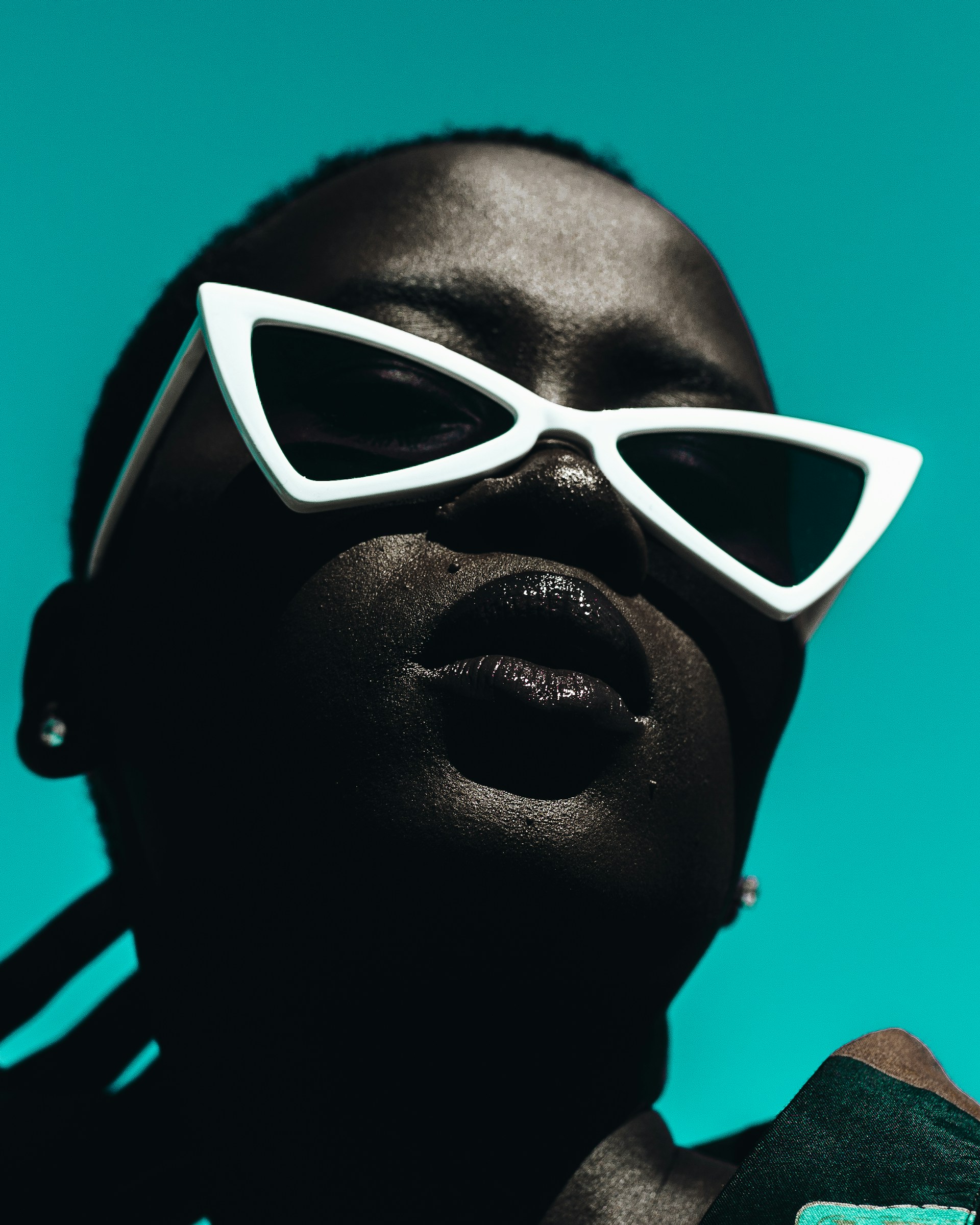 Close-up of a person wearing white triangle sunglasses on a teal background.