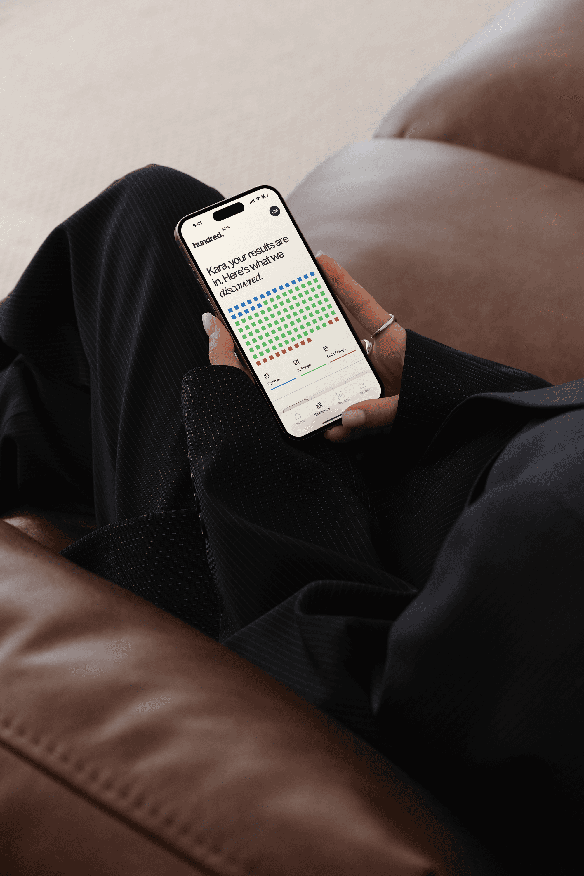 Person holding a phone showing the Hundred app with color-coded biomarker results.