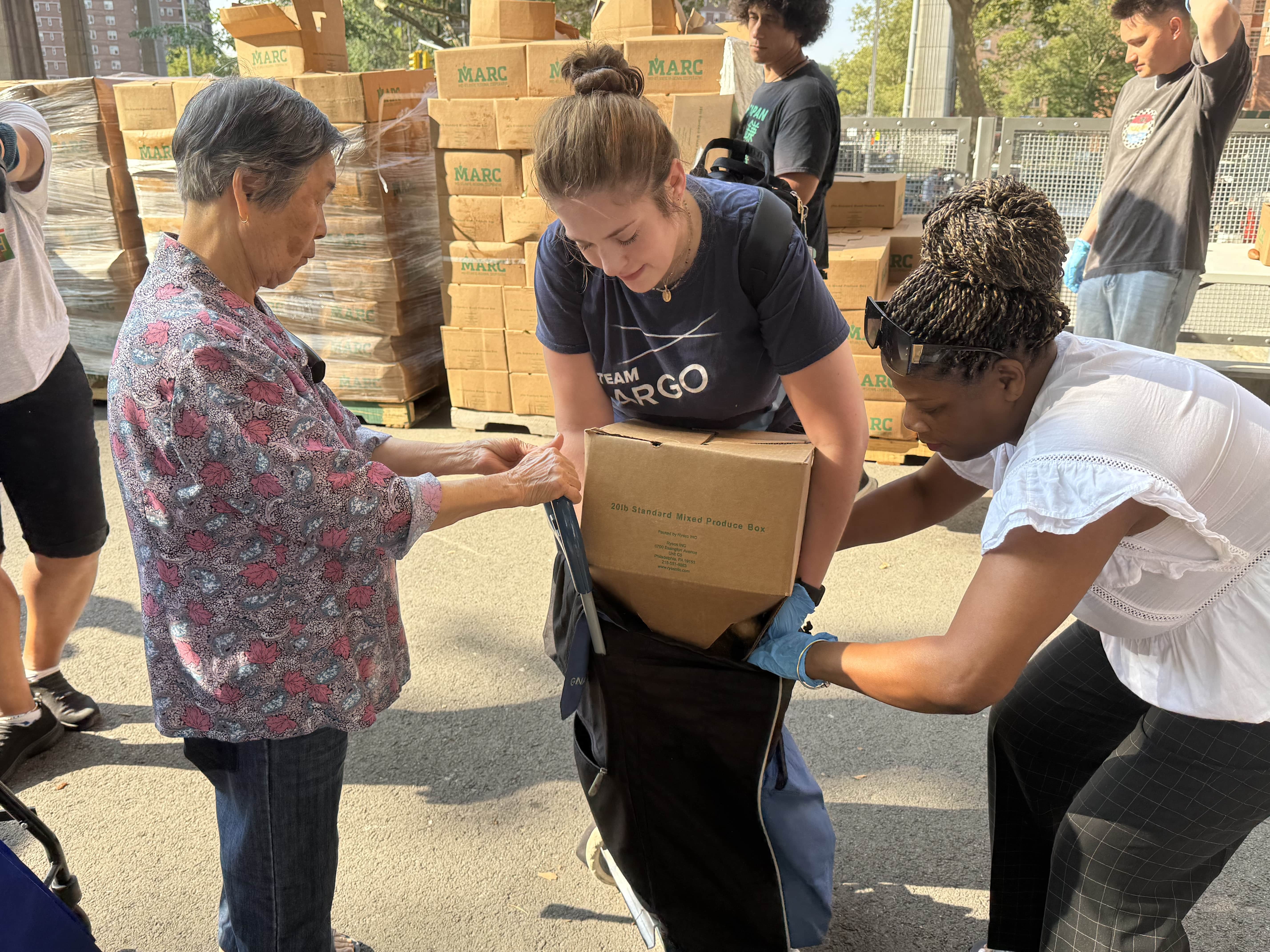 Two volunteers help an older woman store food from the pantry in her bag.