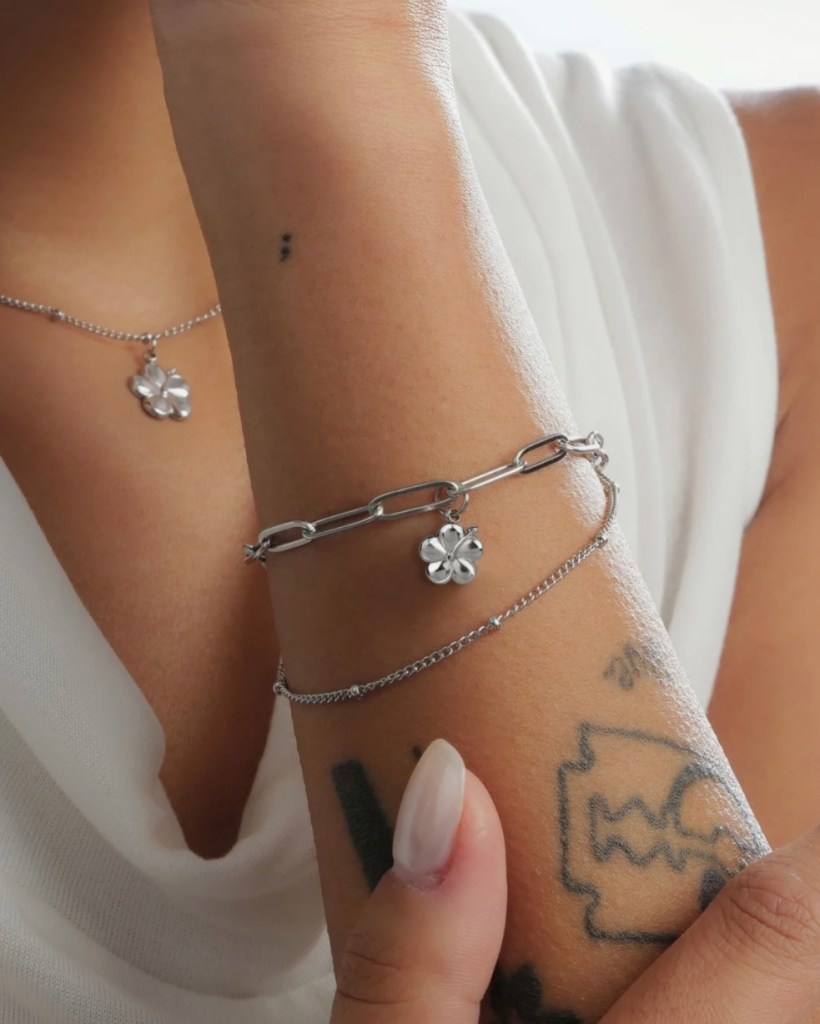 A close-up of a hand wearing a silver bracelet and a necklace featuring a Hibiscus flower charm, highlighting personal jewelry pieces.