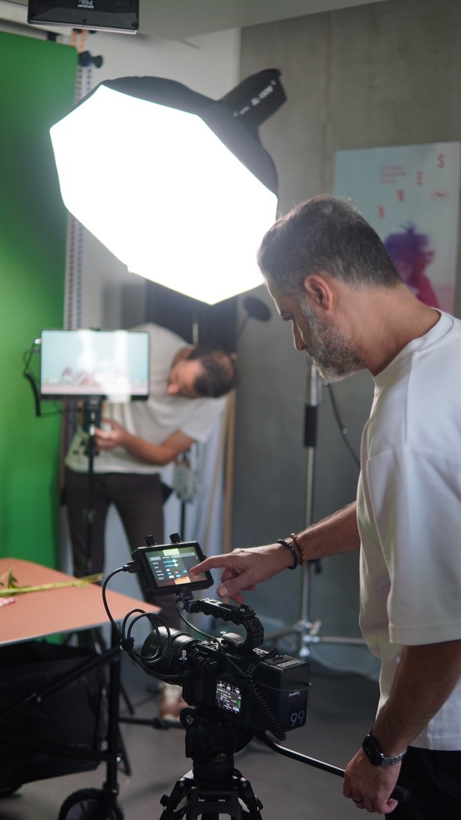 A man sets up professional camera equipment in a studio with a bright softbox light and a green screen, preparing for a photo or video production.