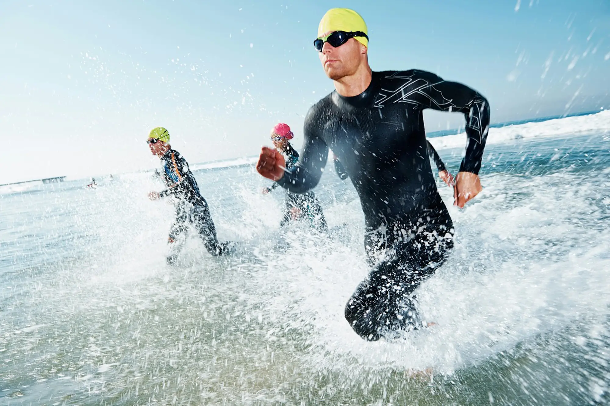 Triathletes exiting the ocean swim at the start of a sub 10 hour Ironman attempt, in wetsuits and coloured swim caps