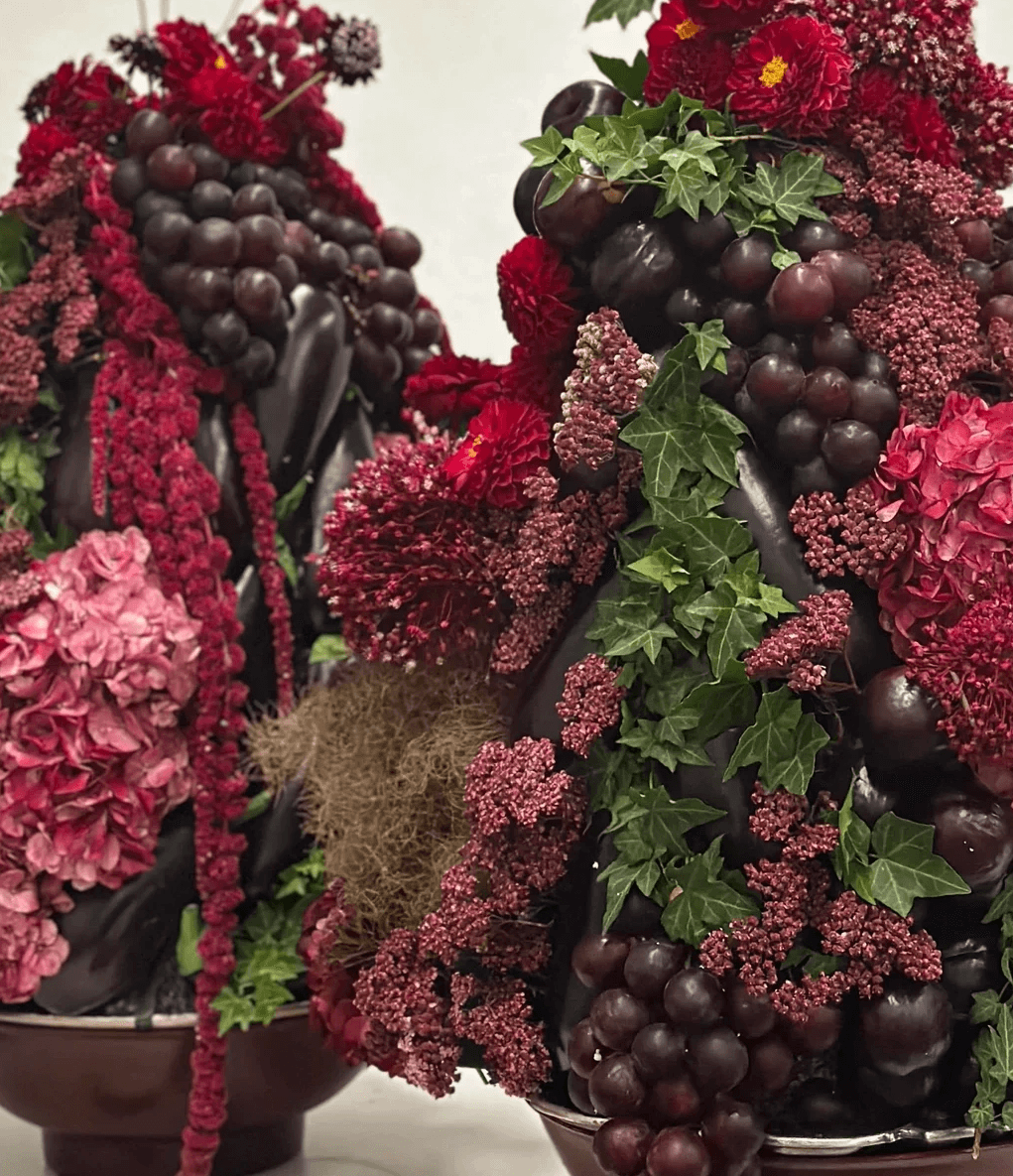Primer plano de arreglos barrocos mezclando flores bordó, frambuesa, hiedra y frutas frescas.