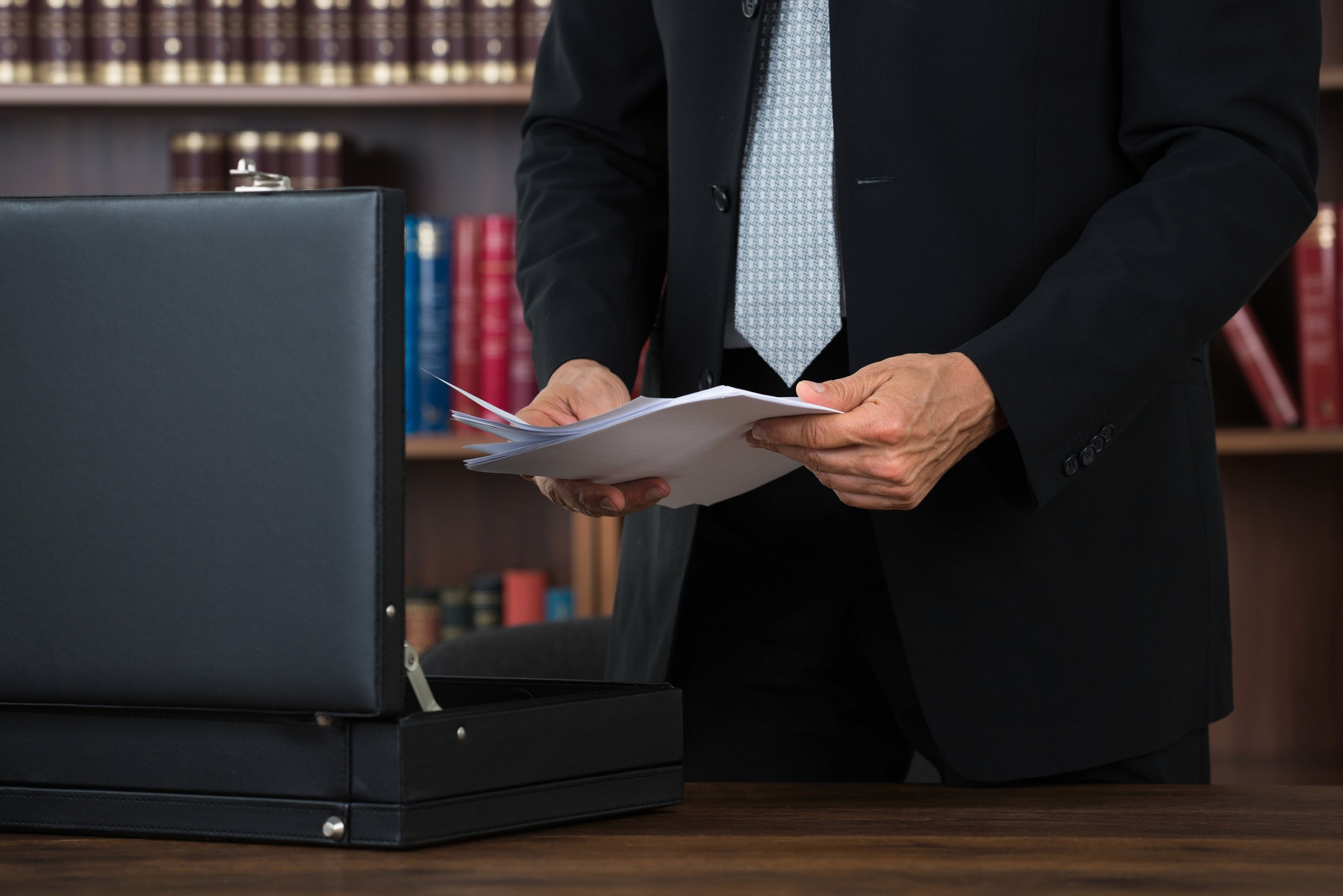 Midsection of male lawyer keeping documents in briefcase at table in office