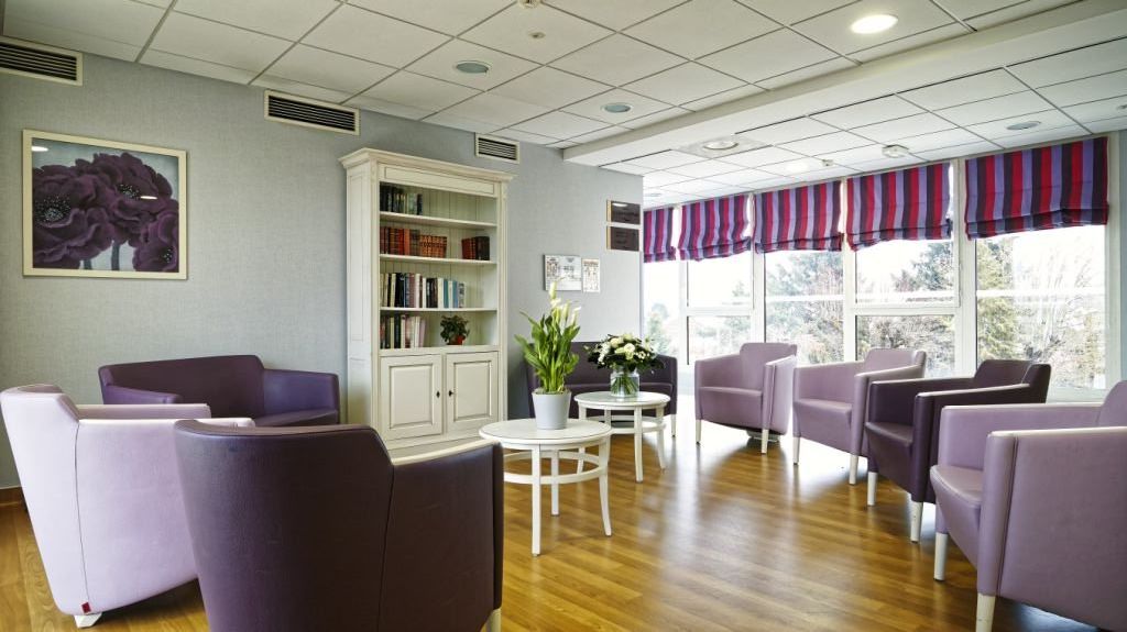 Bright lounge with purple armchairs white coffee tables bookshelf striped window blinds and wood flooring