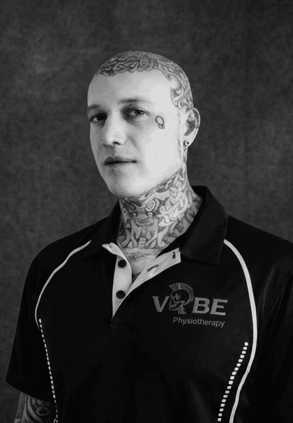 A serene outdoor seating area with two chairs, surrounded by lush greenery and a glassed-in structure.