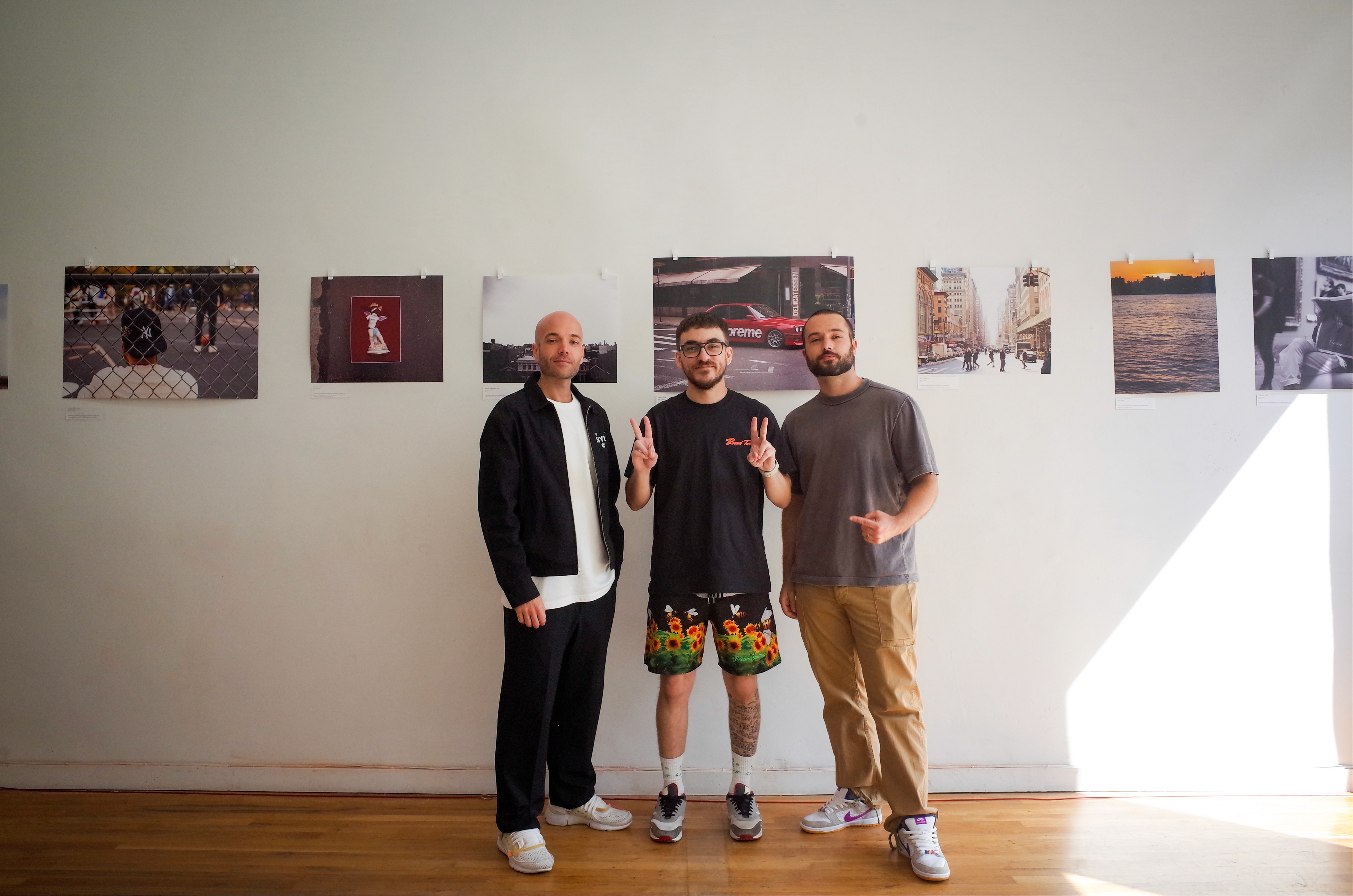 Nick TK Pinto standing with two guests in front of the “New York Narratives” photo wall in a bright gallery space.