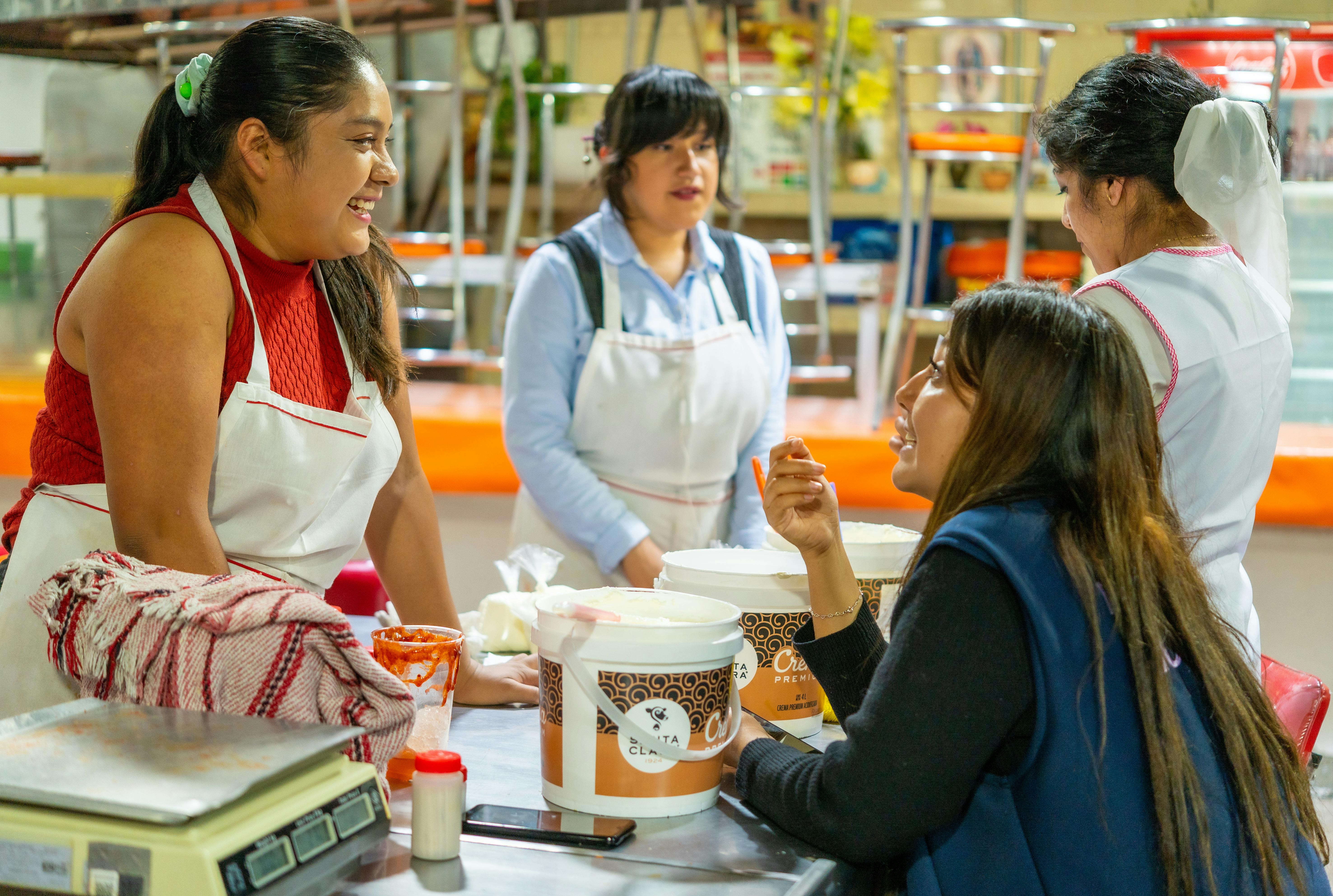 Gruppo di donne che ridono e collaborano in una cucina, simbolo di lavoro di squadra, dialogo e inclusione.