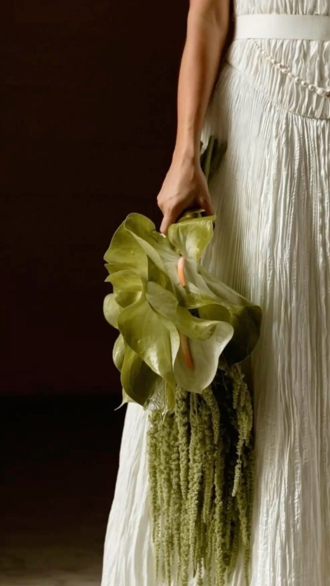 Editorial still life of sculptural green calla lilies held against a muted backdrop — refined, tactile, modern.