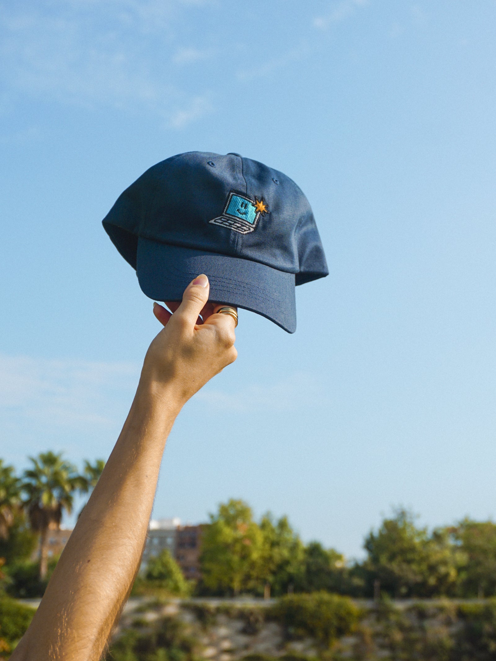 Person holding a blue cap with a logo against a clear sky