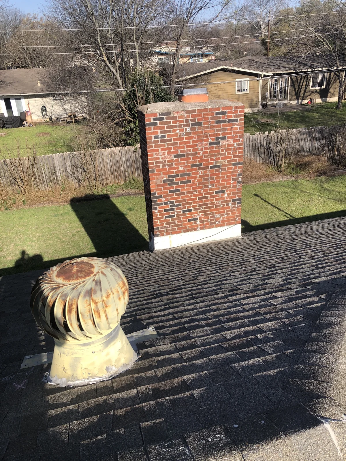 Earlier asphalt shingles and a turbine vent beside the same distinctive red-brick chimney.